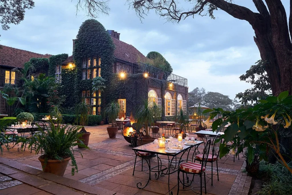 Outdoor garden at Giraffe Manor, with manicured lawns, blooming flowers, and giraffes grazing peacefully in the background.